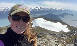 Lucy Boyce hiking in Alaska with snow covered mountains and water in the background